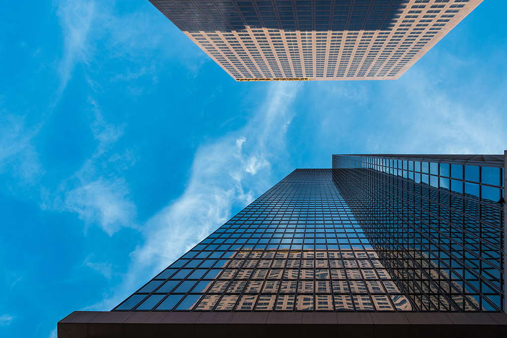 Ground-level perspective of two tall buildings, emphasizing their impressive height and architectural design
