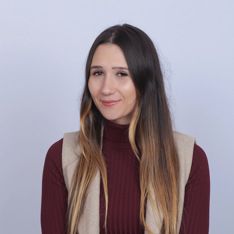 Long hair, casual outfit, neutral background.